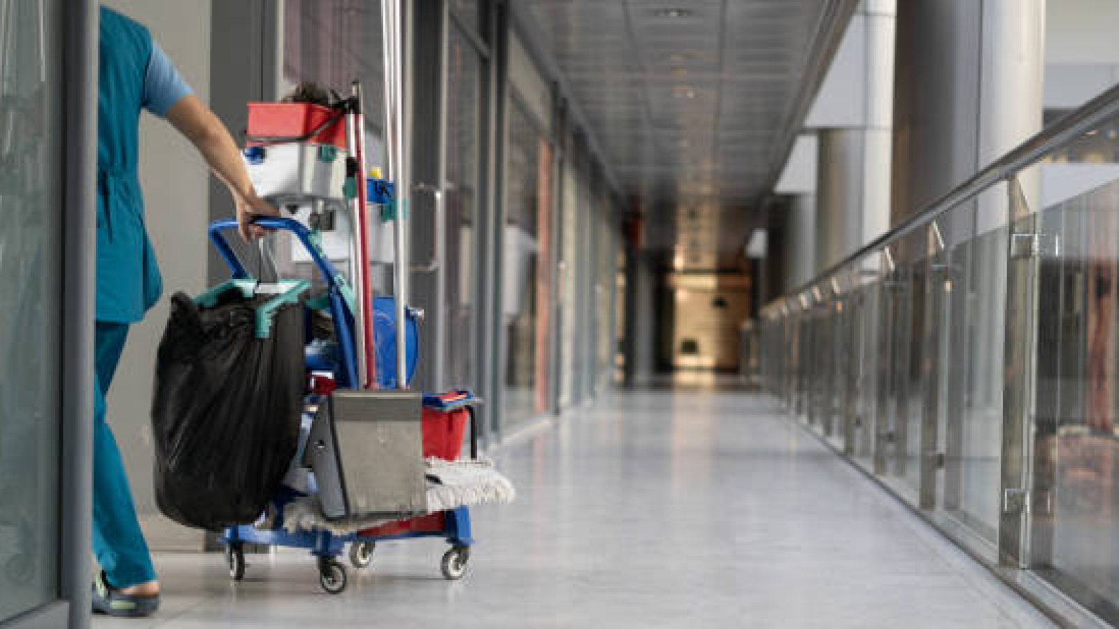 An employee pulls a trolley for cleaning offices. Woman cleaner is engaged in work. Shopping center place for text
