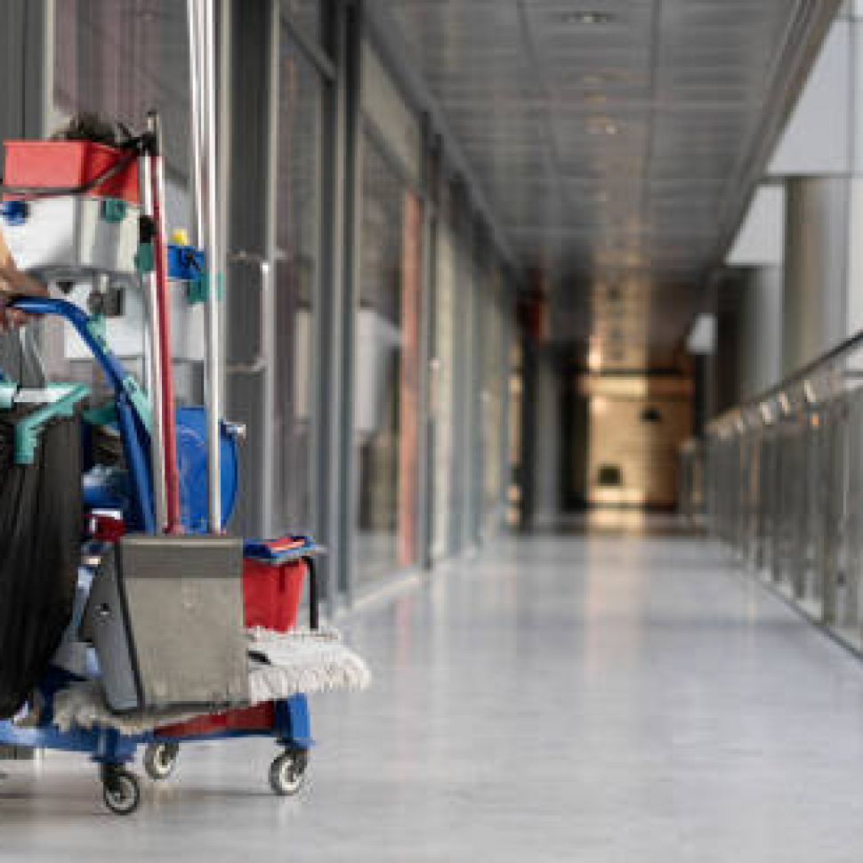 An employee pulls a trolley for cleaning offices. Woman cleaner is engaged in work. Shopping center place for text